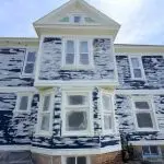 A large older two-story home with heavily peeling exterior paint scraped back to bare wood and primer during prep work, showing what happens when exterior paint reaches the end of how long it lasts.