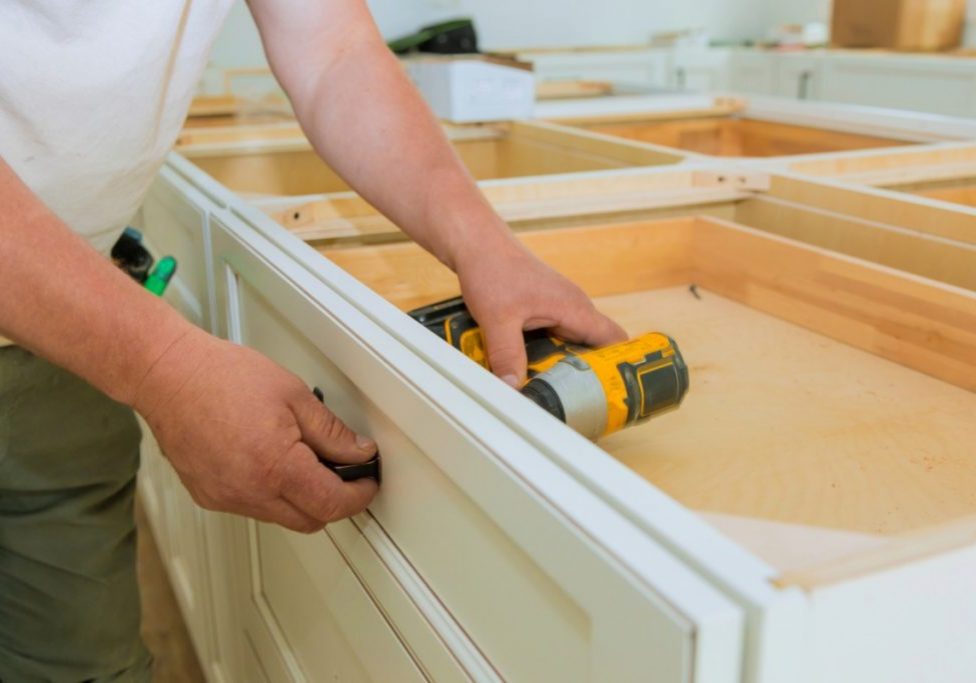 Stahl Painting worker uses a cordless drill to fasten a handle onto a white drawer front while installing new cabinetry, one path to consider when replacing kitchen cabinets.